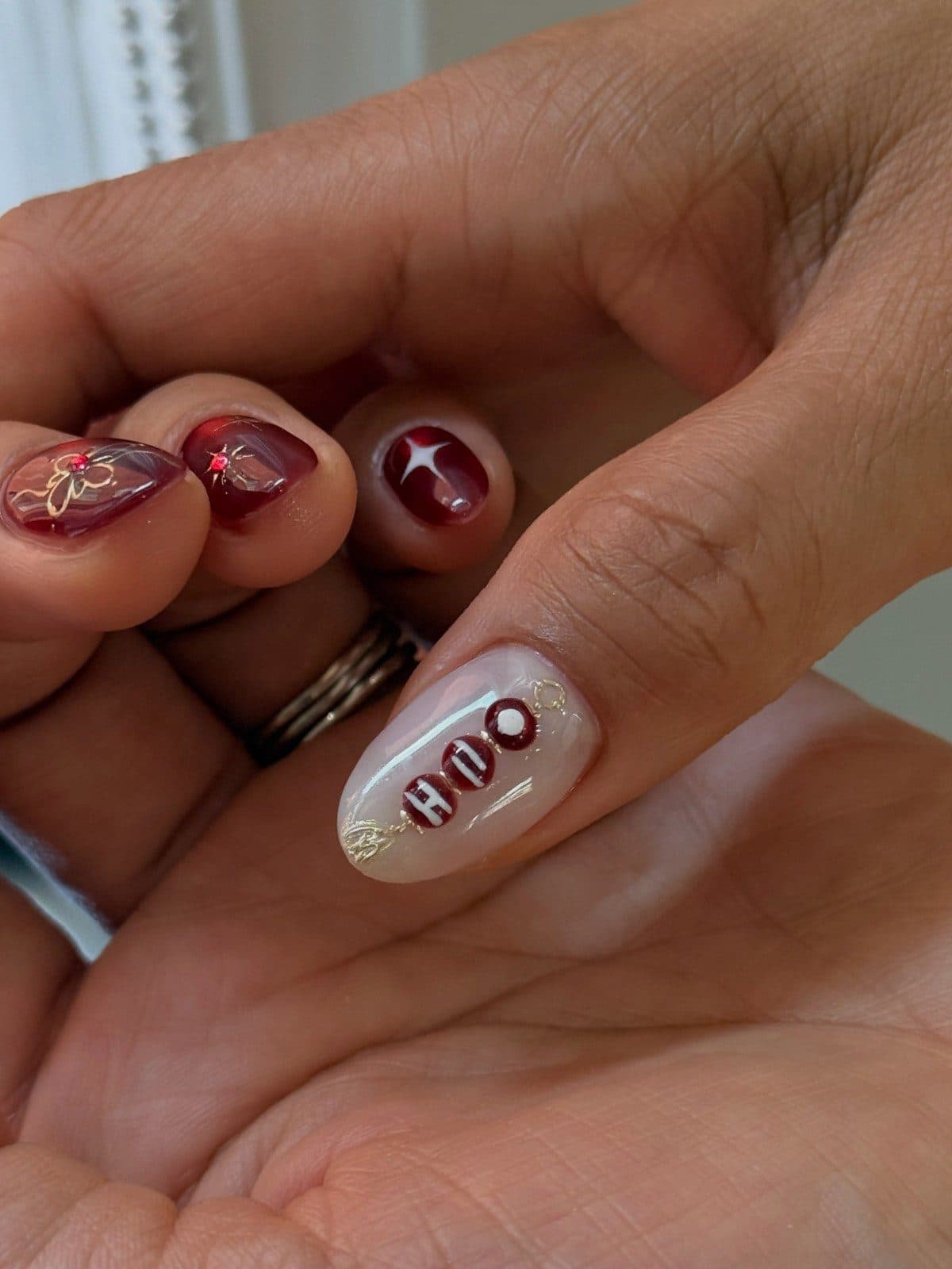 Burgundy and pearl white Korean gel nails with hand-painted lettering and star art by Joy Nail Studio Vancouver